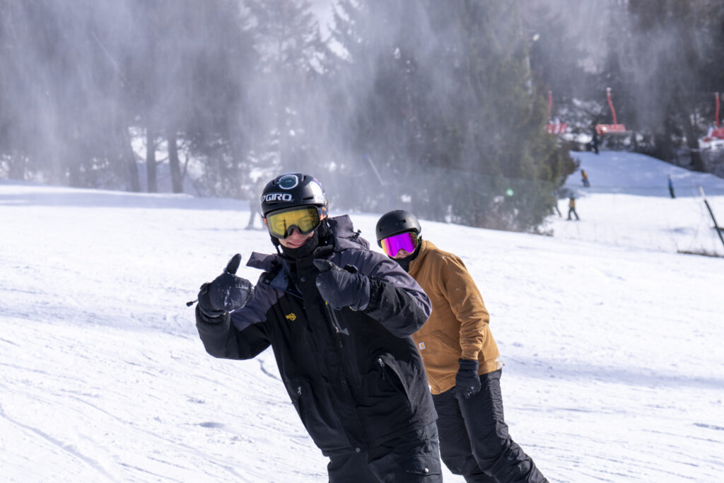 A snowboarder gives a thumbs-up to the camera on the slopes